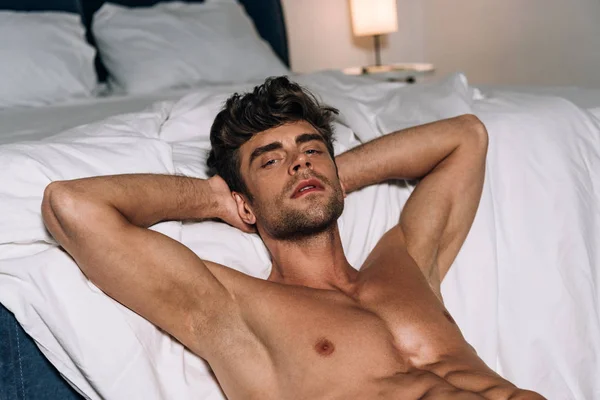 Yakışıklı Üstsüz Bir Adam Yatağın Yanında Yatarken Kameraya Bakıyor — Stok fotoğraf