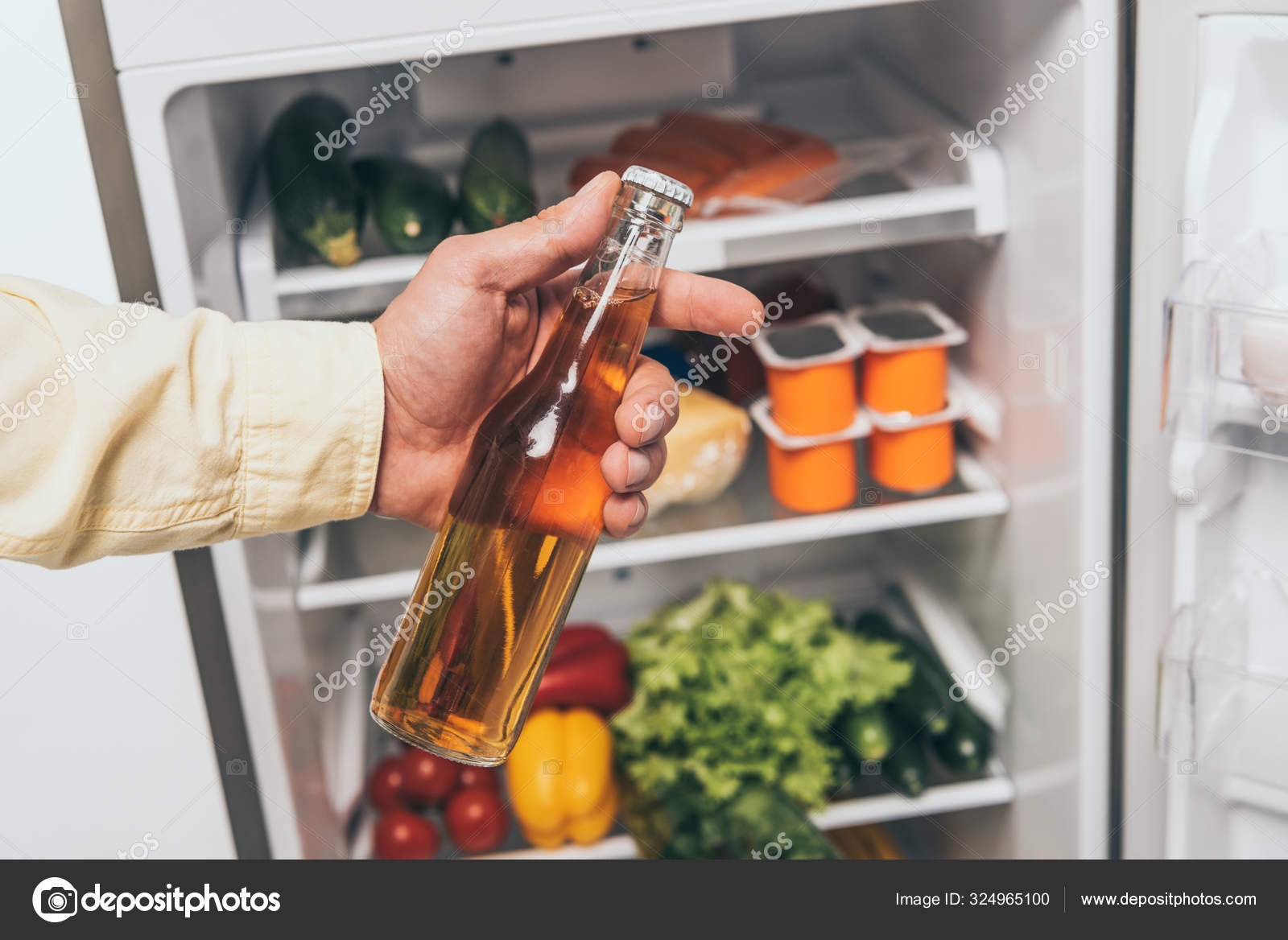 vista recortada del hombre sosteniendo botella de cerveza cerca de nevera abierta llena de alimentos 324965100