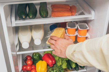 cropped view of man taking cheese out of fridge full of food clipart