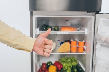 Kırpılmış insan görüntüsü açık buzdolabının yanında baş parmağını gösteriyor beyazı izole edilmiş yiyeceklerle dolu