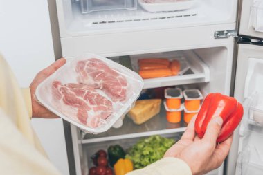 Donmuş et ve taze dolmalık biber taşıyan bir adamın açık buzdolabı dolusu yiyecekle dolu görüntüsü.