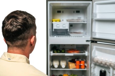 Buzdolabı açık, beyaz yiyeceklere bakan adam.