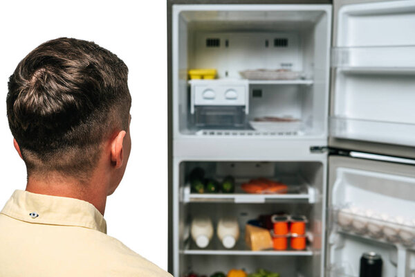 парень смотрит на открытый холодильник с едой изолированы на белом
