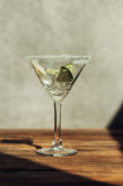 Martini sklenice s ledem, citrónem a limetkou zdobená cukrem na dřevěném povrchu ve slunečním světle