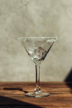Ahşap yüzeyde gün ışığında buzla süslenmiş martini bardağı.
