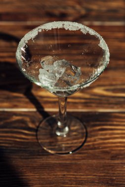 Ahşap yüzeyde gün ışığında buzla süslenmiş martini bardağı.