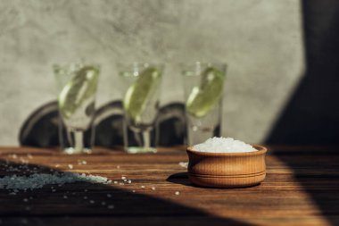 Kase içindeki tuzdan seçici bir odak ve güneş ışığında ahşap yüzeyde limonlu taze tekila.