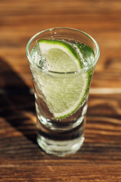 закрытый вид на свежую текилу с известью на деревянной поверхности при солнечном свете
