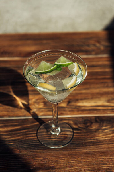 margarita glass with ice, lemon and lime decorated with sugar on wooden surface in sunlight
