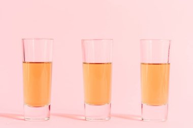 three shots with alcohol in row on pink background clipart