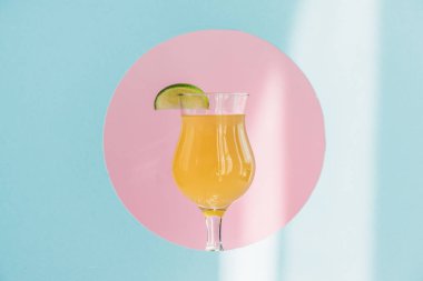 Taze sarı limonata, pembe daire şeklinde, mavi arka planda, güneş ışığında.