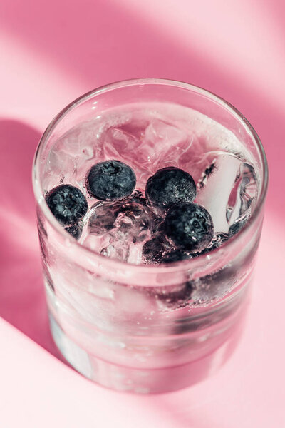 fresh lemonade with ice and blueberries in sunlight on pink background