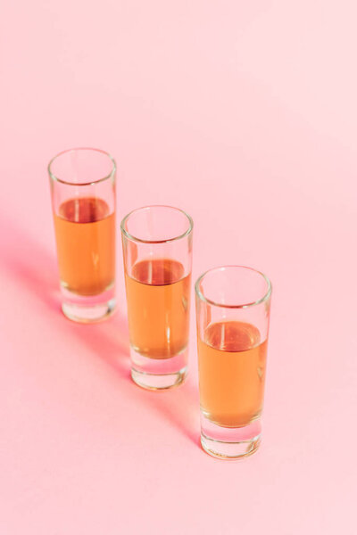 three shots with alcohol in row on pink background