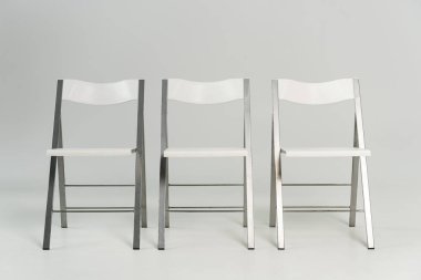 Three modern white chairs on grey background clipart