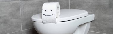 Panoramic shot of toilet paper with smile sign on white toilet bowl in bathroom clipart