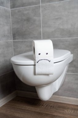 Sad emoticon on toilet paper on ceramic toilet bowl in bathroom clipart