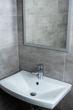 Modern tuvalette aynalı seramik lavabo ve gri fayanslar.