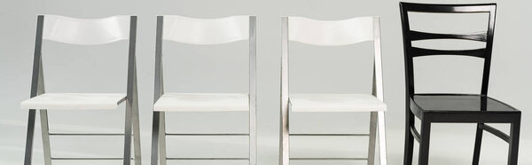 Panoramic shot of white and black chairs on grey background