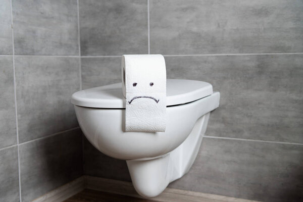 Toilet paper with sad emoticon on toilet bowl in modern restroom