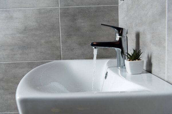 Water flow from sink to ceramic washbasin with plant in modern restroom