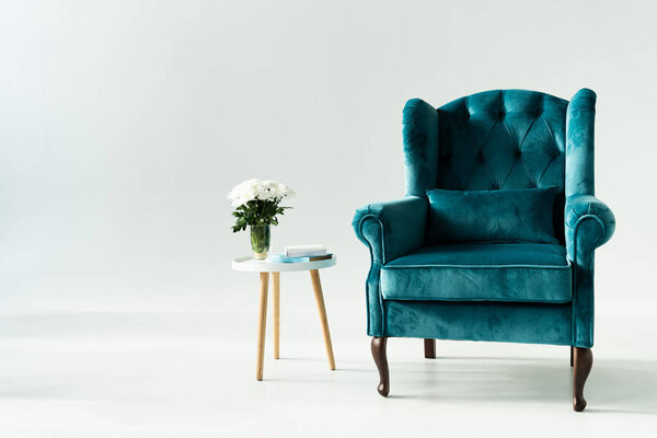 Turquoise armchair by coffee table with flowers and books on grey background
