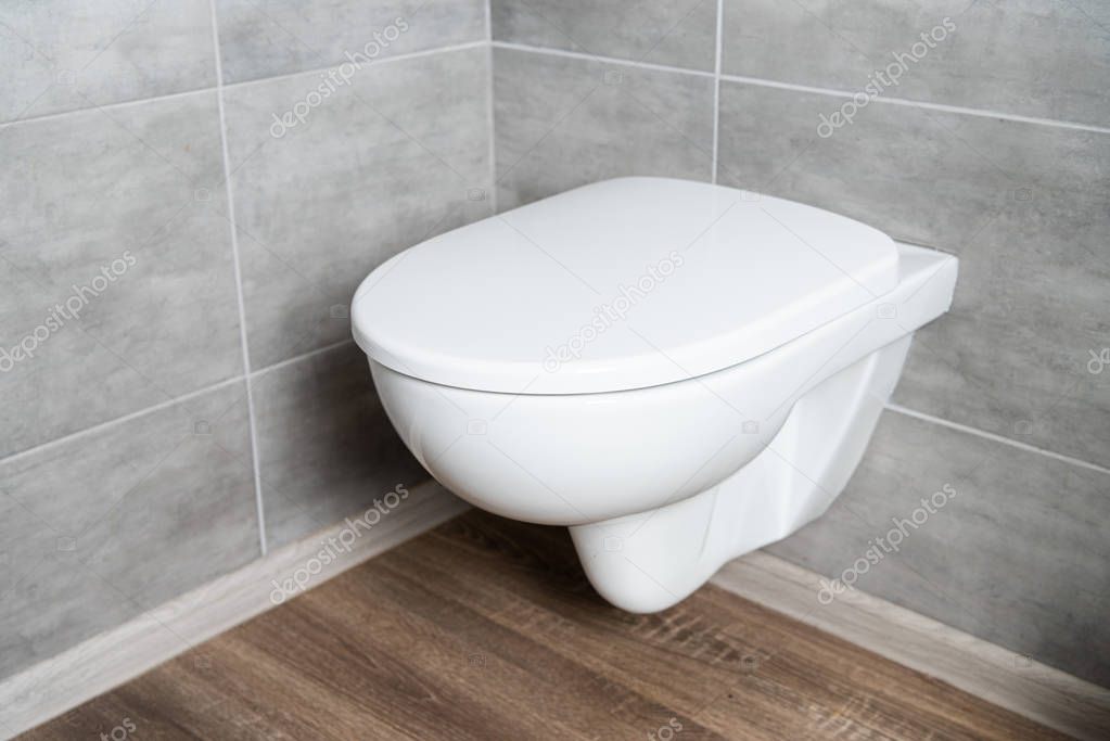 Clean white toilet bowl in restroom with grey tile