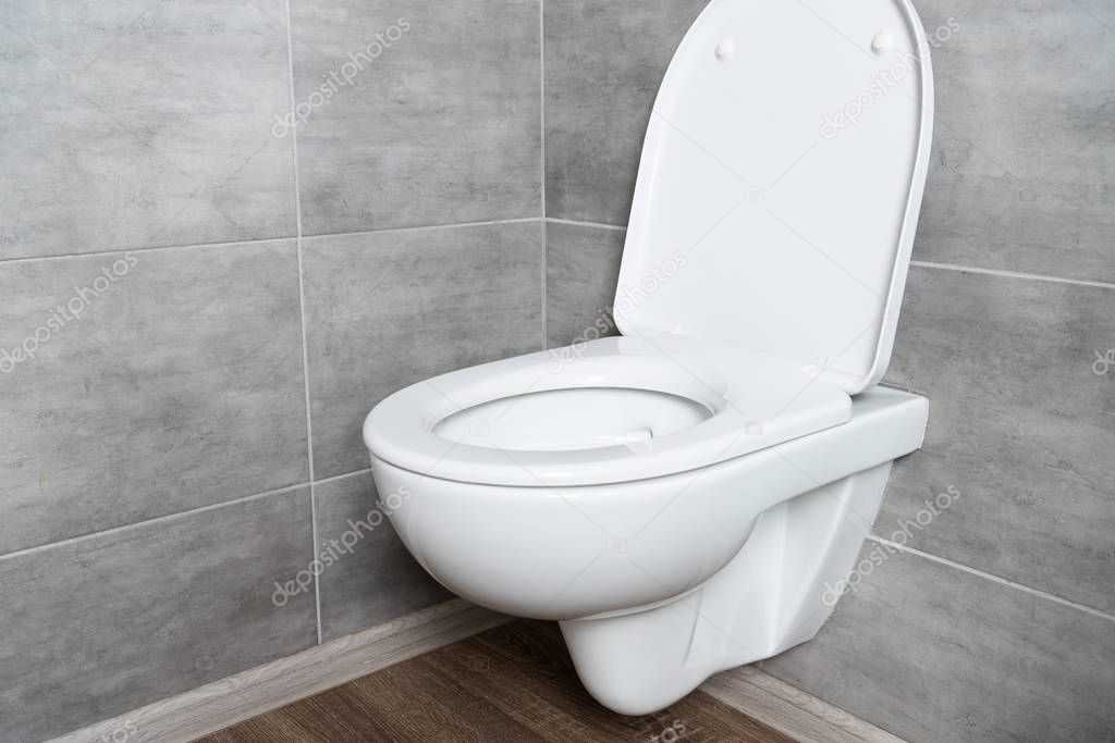 Clean toilet bowl with open seat in modern bathroom with grey tile