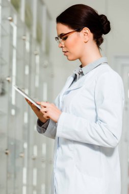 Eczanede dijital tablet kullanan güzel eczacının yan görüntüsü