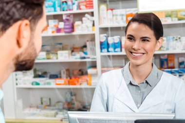 Selective focus of druggist smiling to customer at pharmacy counter clipart
