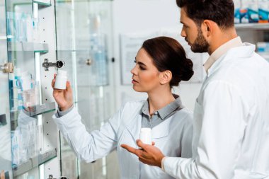 Eczacıların eczane vitrininden aldığı haplarla kavanoza bakması.