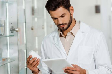İlaç kavanozunu tutarken dijital tablet kullanan yakışıklı bir eczacı. 