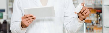 Dijital tablet ve kavanozu haplarla, panoramik çekimle tutan eczacının kırpılmış görüntüsü