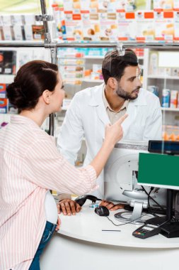 Pregnant customer pointing at medicaments to pharmacist in drugstore clipart