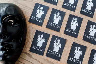 KYIV, UKRAINE - NOVEMBER 22, 2019: top view of playing cards with mafia letters near black party masks  clipart