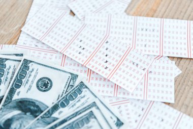 İşaretli piyango biletlerinin en üst görüntüsü ahşap masadaki dolar banknotlarının yanında.