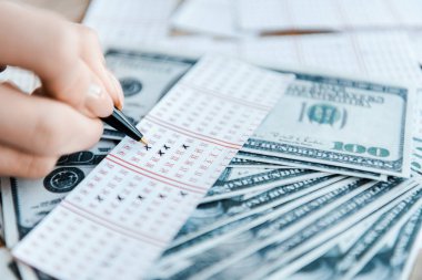 Piyango biletinin üzerinde dolar banknotlarının yanında rakamları işaretleyen kadın manzarası 