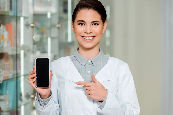 Farmacéutico Sonriente Apuntando Con Dedo Teléfono Inteligente Con Pantalla Blanco —  Fotos de Stock