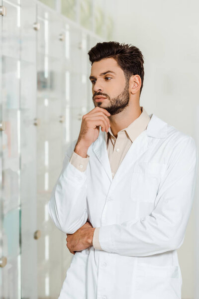 Thoughtful pharmacist looking at showcase in drugstore