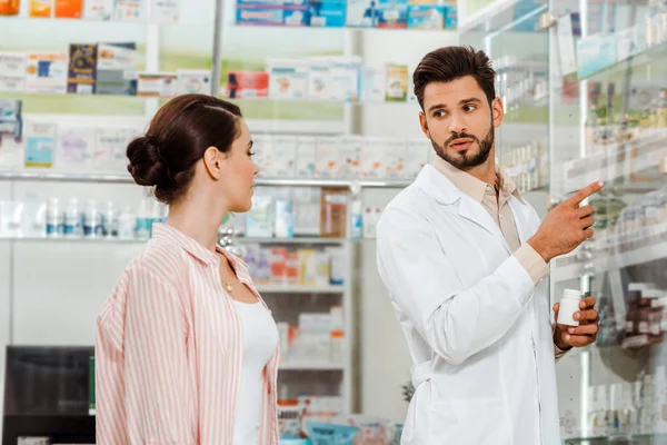 Gyógyszerész Tablettákkal Ujjal Mutogatott Polcokra Gyógyszerekkel Ügyfélnek — Stock Fotó