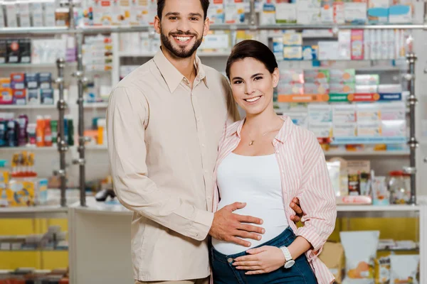 男人笑着拥抱怀孕的妻子 在药店看着相机 — 图库照片