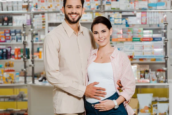 Uomo Sorridente Che Abbraccia Moglie Incinta Guarda Fotocamera Farmacia — Foto Stock