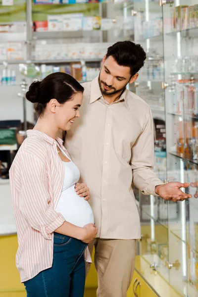 男人指着药店的橱窗对着笑着的孕妇 — 图库照片