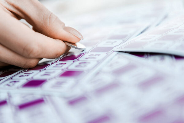 selective focus of woman holding coin and scratching lottery ticket 