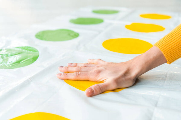 KYIV, UKRAINE - NOVEMBER 22, 2019: cropped view of woman putting hand on yellow circle while playing twister game 