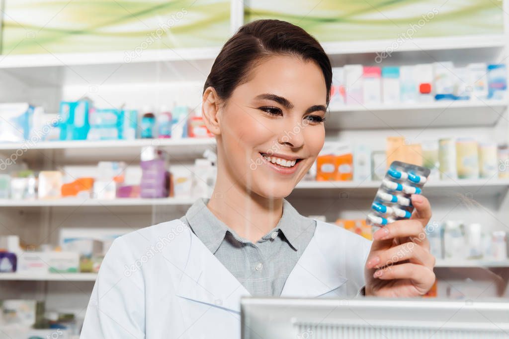 Beautiful smiling pharmacist holding blister with pills in drugstore