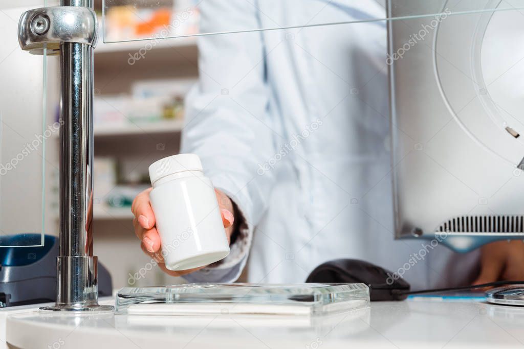 Cropped view of female pharmacist putting jar with pills on counter