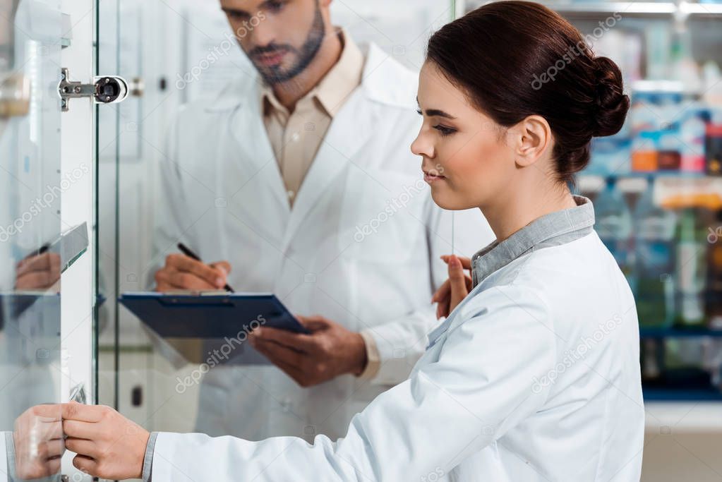 Selective focus of pharmacists with clipboard beside showcase in pharmacy