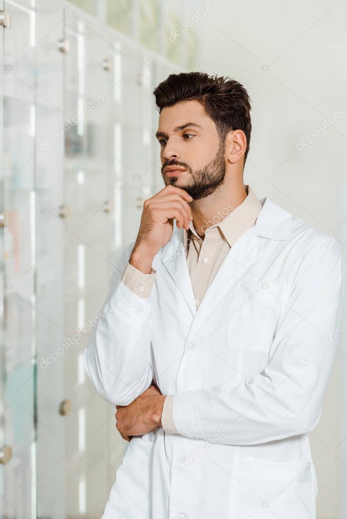 Thoughtful pharmacist looking at showcase in drugstore