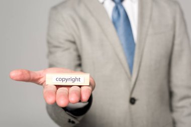 cropped view of businessman showing wooden block with word copyright isolated on grey clipart