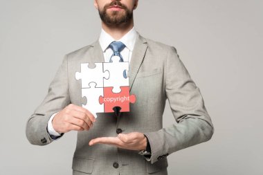 Telif hakkı yazıları gri renkli yapboz tutan işadamının kırpılmış görüntüsü